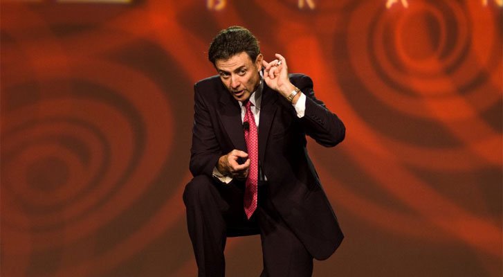 Image: Coach Rick Pitino speaks in front of a conference audience. Conference and event speaker selection services by Benchmarc360.
